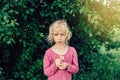 cute beautiful blonde Caucasian girl in red pink dress holding white daisy flower in her hands. Royalty Free Stock Photo