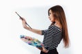 Cute beautiful girl artist holding a palette and brush in the process draws inspiration. White background, isolated. Royalty Free Stock Photo