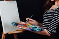 Cute beautiful girl artist painting a picture on canvas an easel. Space for text. Studio black background. Royalty Free Stock Photo