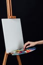 Cute beautiful girl artist painting a picture on canvas an easel. Space for text. Studio black background. Royalty Free Stock Photo