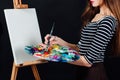 Cute beautiful girl artist painting a picture on canvas an easel. Space for text. Studio black background. Royalty Free Stock Photo