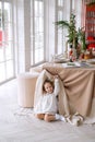 A cute beautiful girl is hiding under Christmas table behind the tablecloth Royalty Free Stock Photo