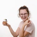 Cute beautiful happy teen girl with glasses holds cream cake in hand and smiles on white background Royalty Free Stock Photo