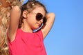 Cute beautiful kid girl in fashion sunglasses looking and relaxing near the palm on blue sea and sky background Royalty Free Stock Photo