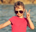 Cute beautiful kid girl in fashion sunglasses showing v sign making the selfie on blue sea and sky background. Closeup toned port Royalty Free Stock Photo