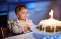 Cute beautiful little baby girl celebrating first birthday. Child blowing one candle on homemade baked cake, indoor Royalty Free Stock Photo