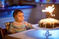 Cute beautiful little baby girl celebrating first birthday. Child blowing one candle on homemade baked cake, indoor Royalty Free Stock Photo