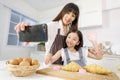 A cute and beautiful mother with young and little daughter, 7 years old, taking a selfie photo with a smartphone in modern kitchen Royalty Free Stock Photo