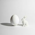 Cute beautiful porcelain Easter bunny sitting beside large elegant white egg on pure white background Royalty Free Stock Photo