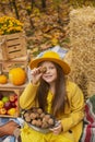 Cute beautiful teenage brunette girl in an orange hat, dress and coat holding a walnut near her face and a basket with walnuts