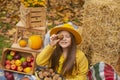 Cute beautiful teenage brunette girl in an orange hat, dress and coat holding a walnut near her face and a basket with walnuts