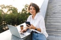 Cute beautiful woman standing outdoors using laptop computer chatting by phone Royalty Free Stock Photo