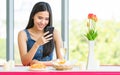 A cute beautiful young Asian woman sitting alone at a desk in a restaurant with a smartphone in hand Royalty Free Stock Photo