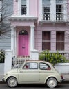 Beige vintage Fiat 500 classic car parked in front of a house with a pink door in Notting Hill, west London UK. Royalty Free Stock Photo