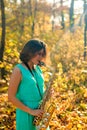 Cute black-haired girl in a blue dress plays the yellow saxophone in the autumn forest