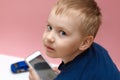 Cute blond baby boy with blue eyes holding mobile phone in hands and making video shooting of toy car. Funny face expression of yo Royalty Free Stock Photo