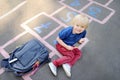 Cute blond boy playing hopscotch game after school with bags laying near Royalty Free Stock Photo