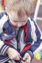 Cute blond caucasian baby boy tries to fasten the zipper the jacket.