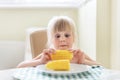 Cute blond caucasian girl holding in hand tasty boiled sweet corn cob and lokking on it with amazed wide opened eyes. Child loves Royalty Free Stock Photo