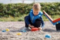 A cute blond child is playing with sand toys near the balance swing in the yard. Safe surface with of small pebbles in playground