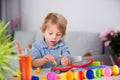 Cute blond child, boy, playing with play doh modeline at home, making different objects