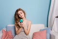 Cute blond girl with curly hair sitting on a sofa and holding a blue cupcake. Colorful pillows on the sofa. Girl looks Royalty Free Stock Photo