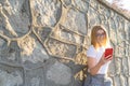 Cute Blond girl with glasses lying on a stone wall playing to a game in her smart phone. Student teenager with white shirt