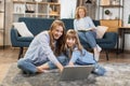 Cute blond girls sisters sitting on warm floor play at home together using laptop Royalty Free Stock Photo