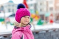 Cute blond kid girl portrait wearing pink knitted hat and sport skiing jacket having fun at playground outdoor during cold winter Royalty Free Stock Photo