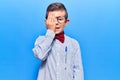 Cute blond kid wearing nerd bow tie and glasses covering one eye with hand, confident smile on face and surprise emotion Royalty Free Stock Photo