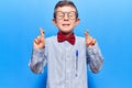 Cute blond kid wearing nerd bow tie and glasses gesturing finger crossed smiling with hope and eyes closed Royalty Free Stock Photo