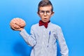 Cute blond kid wearing nerd bow tie and glasses holding brain scared and amazed with open mouth for surprise, disbelief face Royalty Free Stock Photo