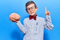 Cute blond kid wearing nerd bow tie and glasses holding brain smiling with an idea or question pointing finger with happy face, Royalty Free Stock Photo