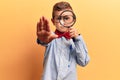 Cute blond kid wearing nerd bow tie and glasses holding magnifying glass with open hand doing stop sign with serious and confident Royalty Free Stock Photo