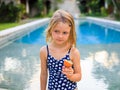 Cute blond little girl in blue swimsuit sitting at the swimming pool, holding passion fruit. Enjoy eating tropical fruit. Summer Royalty Free Stock Photo