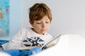 Cute blond little kid boy in pajamas reading book in his bedroom Royalty Free Stock Photo