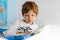 Cute blond little kid boy in pajamas reading book in his bedroom. Excited child reading loud, sitting in his bed Royalty Free Stock Photo