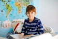 Cute blond little kid boy in pajamas reading book in his bedroom. Excited healthy child reading loud, sitting in his bed Royalty Free Stock Photo