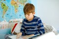 Cute blond little kid boy in pajamas reading book in his bedroom. Excited healthy child reading loud, sitting in his bed Royalty Free Stock Photo