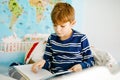 Cute blond little kid boy in pajamas reading book in his bedroom. Excited healthy child reading loud, sitting in his bed Royalty Free Stock Photo