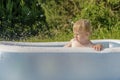 Cute blond little toddler kid boy having fun playing splashing water in inflatable pool on private backyard during heat.Summer Royalty Free Stock Photo