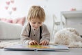 Cute blond preschool child, blond boy with pet maltese dog, reading book at home with mother Royalty Free Stock Photo