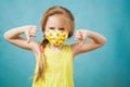 Cute blond preteen girl in antiviral medical mask shows stop gesture.