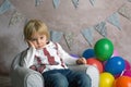 Cute blond toddler child, boy, sitting on little baby armchair, playing with colorful balloons Royalty Free Stock Photo