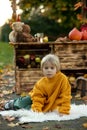 Cute blond toddler child and sibling brothers, standing next to autumn wooden stand with decoration, apples, leaves, mug,
