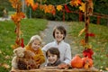 Cute blond toddler child and sibling brothers, standing next to autumn wooden stand with decoration, apples, leaves, mug,