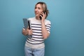 cute blond woman talking on the phone holding a laptop in her hands on a blue background with copy space Royalty Free Stock Photo