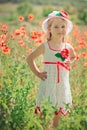 Cute blond young girl child stylish dressed in white handmade hooked dress wearing airy hat top posing on meadow of forest poppy p Royalty Free Stock Photo