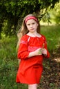 Cute blond young girl posing in a russian traditional red dress near fir tree Royalty Free Stock Photo