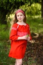 Cute blond young girl posing in a russian traditional red dress near fir tree Royalty Free Stock Photo